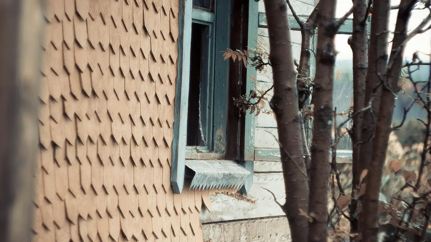 Weathered exterior of an older house with a damaged window